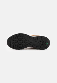 Suela de zapatilla de goma negra con un patrón texturizado, que cuenta con una amortiguación en la entresuela y un logo de Timberland grabado. Acento verde cerca del talón.