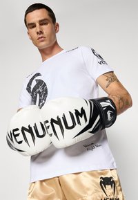 Balds Venum t-krekls ar melnu marmora apdruku un logo. Modelis tur baltas boksa cimdi ar melniem akcentiem un punktveida burtiem.