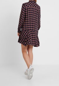 Marinblå och röd rutigt skjortklänning med utsvängd nederkant, långa ärmar och krage, tillverkad av ett mjukt tyg. Bärs med vita sneakers.