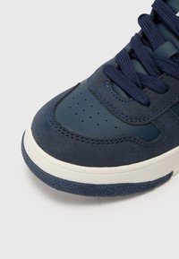 Baskets bleu marine en matériau en daim et cuir, bout arrondi, languette rembourrée, design perforé sur la boîte à orteils et semelle en caoutchouc blanche contrastante.