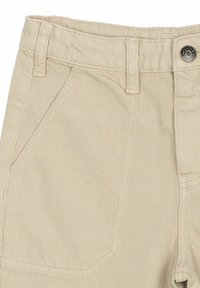 Beige pamutnadrág lapos elülső részes, átlós oldalsó zsebekkel, látható varrással és fém gombos zárással.