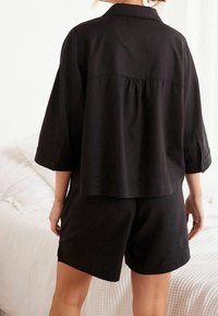 Czarna lniana koszula o luźnym kroju, z krótkimi rękawami i zapięciem na guzik. Połączona z pasującymi czarnymi szortami, obie części o prostym wzornictwie.