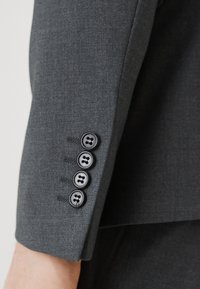 Gray blazer sleeve features four black buttons, smooth texture, subtle herringbone pattern, and clean stitching detail.