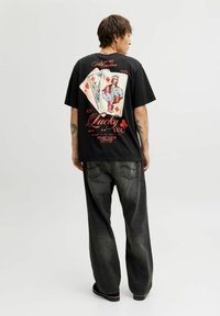 Zwarte graphic t-shirt met speelkaarten en de tekst "Lucky You", gecombineerd met donkere baggy jeans. De stof lijkt zacht en casual van ontwerp.