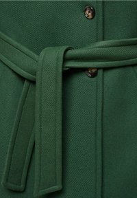 Manteau en laine vert foncé avec ceinture en tissu nouée et deux boutons noirs visibles sur la fermeture avant.