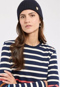 Marine-blauwe geribbelde muts met ankerpatch. Gestreepte crewneck sweater in marineblauw en crème met rode accenten, met zichtbare naden en lange mouwen.