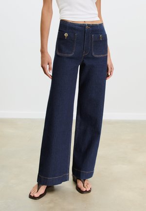 Dark blue wide-leg jeans made of denim, featuring two front pockets, brass hardware accents, and contrasting stitching along the seams.