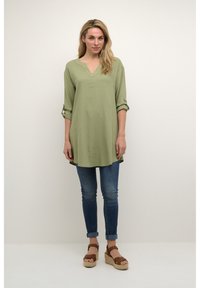 Olivno zelena tunika z V-izrezom, z rokavi do tri četrtine, zavihani. Ujemajoče se temno modre skinny kavbojke in rjave platforme.