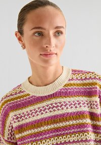 Pull en tricot avec des rayures horizontales en rose, crème et or. Encolure côtelée et motifs texturés sur tout le tissu.