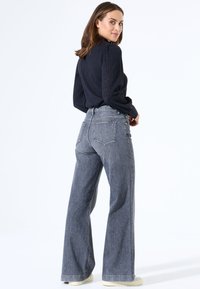Weite, graue Jeans aus Denim mit hohem Bund, dezenten Steppdetails und klassischem 5-Taschen-Design, kombiniert mit einem strukturierten schwarzen Pullover.