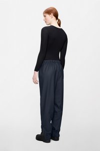 Czarna bluzka z długim rękawem w połączeniu z luźnymi granatowymi spodniami z elastycznym pasem i marszczonymi mankietami; czarne obuwie.