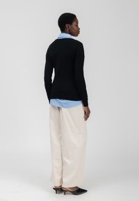 Zwarte gebreide trui over een blauwe gestreepte button-up shirt, gecombineerd met crèmekleurige wijde broekspijpen en zwarte puntige hakken.