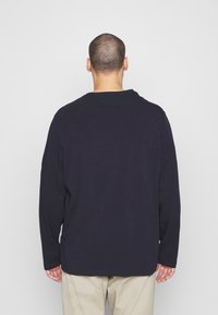 Marinblå långärmad tröja, design med rund hals, lätt tyg, slät textur, något rundad nederkant, i kombination med beiga byxor.