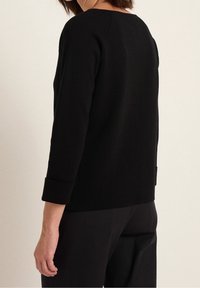 Svart stickad tröja med rund halsringning och trekvartslånga ärmar, med rullade muddar och en enkel, strömlinjeformad design.