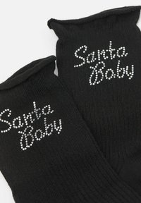 Černé pletené ponožky s žebrovanou texturou, na kterých jsou slova "Santa Baby" ze stříbrných kamínků. Navrženy s přehnutým vrcholem.