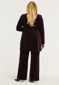 Fluwelen twee-delige outfit in donkerpaars. Langsleeve top en wijde broek. Zachte textuur, met een ontspannen silhouet en minimale details.