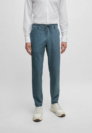 Pantaloni leggeri di colore azzurro con vita regolabile, taglio dritto e tessuto strutturato. Abbinati a sneakers bianche per un contrasto.