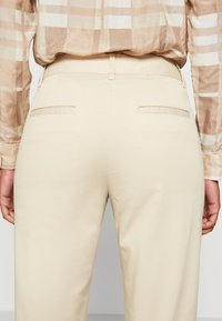 Beiga byxor med en slät yta, med en åtsittande midjeband, två bakfickor och en minimalistisk design.