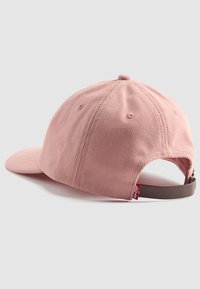 Pink corduroy cap with a curved visor, adjustable back strap, and a small red brand tag on the side. Textured fabric with visible ridges.