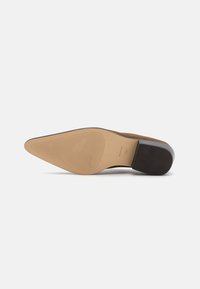 Sko med spiss tå, laget av brunt semsket skinn og med en glatt beige gummisåle. Har teksturerte gripe-linjer på sålens underside.