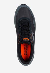 Zapatilla deportiva negra con parte superior texturizada, con acentos grises y marca en color naranja. Diseñada para la comodidad con interior acolchado y suela flexible.