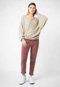 Beige slouchy sweater met een wijde halslijn en lange mouwen, gecombineerd met een stofroze corduroy broek en witte sneakers.