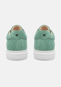 Sneakers in suede verde con suola in gomma bianca, dotati di punta arrotondata, dettagli ondulati sul tallone e un piccolo accento con logo nero.