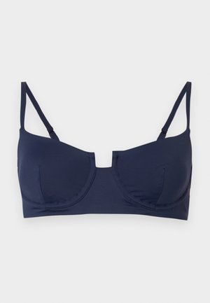 Σουτιέν σε ναυτικό μπλε με μπανέλα, ρυθμιζόμενους λεπτούς ιμάντες ώμου και μικρό κεντρικό άνοιγμα σε απλό φωτεινό υπόβαθρο.