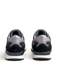 Schwarz-graue Sportschuhe mit Obermaterial aus Wildleder und Mesh, gepolstertem Kragen und weißer Gummisohle mit strukturierten Details.