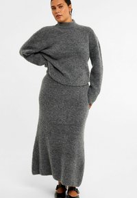 Grå strikket to-delt sæt bestående af en højhalset sweater med lange ærmer og en matchende lang nederdel, begge med en blød, tekstureret overflade.