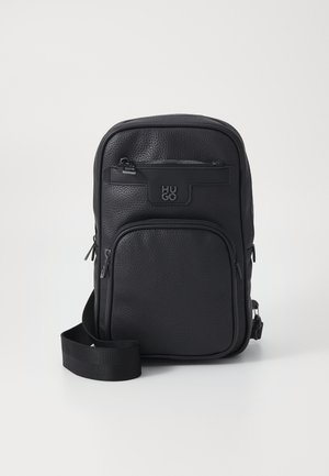 Sac à bandoulière en cuir noir avec une finition texturée, dotée de deux compartiments zippés et d'un logo de marque. Sangle ajustable incluse.