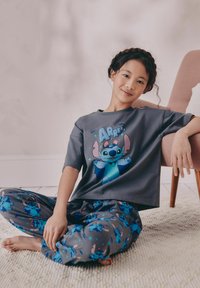Graues Baumwoll-T-Shirt mit einem blauen Comic-Charakter-Design, kombiniert mit grauen Schlafanzughosen, die mit einem sich wiederholenden blauen Charakterdruck versehen sind.