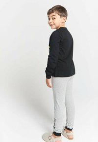 Black long-sleeve shirt with yellow accents, paired with light gray leggings. The outfit features soft fabric and logo detail on the leg.