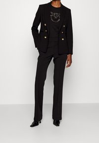 Black blazer with gold buttons, paired with a black top featuring a sequin design, and tailored black trousers. Finished with sleek black heels.