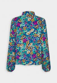 Blouse fleurie présentant un fond bleu foncé vibrant avec des fleurs colorées en rose, orange, vert et turquoise. Manches longues avec poignets froncés.