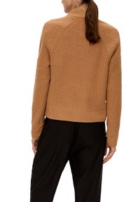 Strickpullover in einem warmen Beigeton, mit strukturiertem Design, geripptem Kragen und taillierter Passform. Getragen zu schwarzen Hosen.