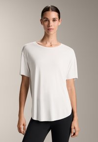 Tricou alb cu mâneci scurte, cu guler rotund și margine curbată, realizat dintr-un material neted și ușor. Purtați cu colanți negri.