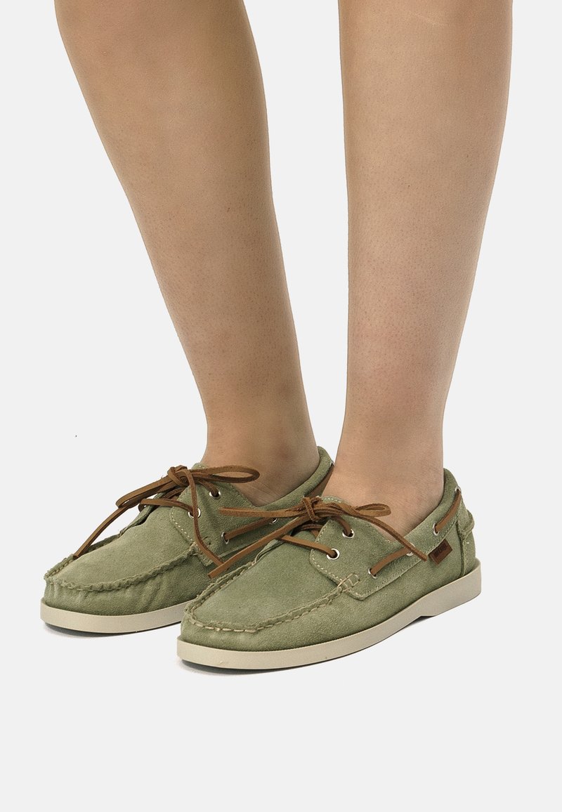 Zapatos náuticos de gamuza verde con cordones y ojetes marrones, presentan un diseño sencillo, punta redonda y suela de goma beige.