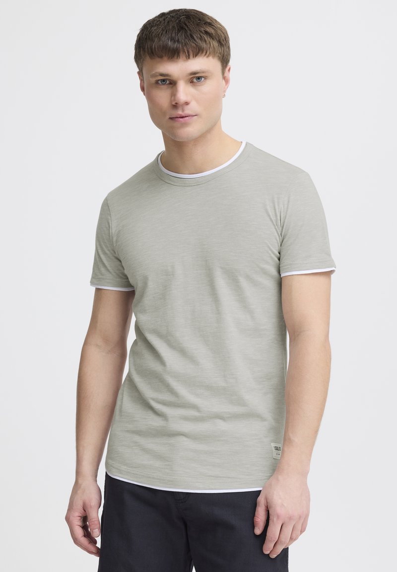 Tricou scurt cu mânecă, de culoare gri deschis, cu guler rotund și margini albe. Fabricat dintr-un material moale, având un model texturat subtil.