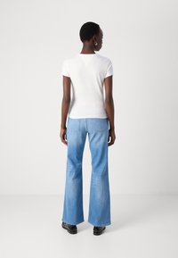 T-shirt bianco a maniche corte abbinato a jeans a zampa d'elefante blu chiaro, con una trama sbiadita e design classico della tasca posteriore. Scarpe nere completano il look.