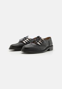 Mustad mustad nahast kingad ümarate varvastega, mis on kaunistatud hõbedaste detailide ja brogue-ornamentikaga, madala kanna ja tekstuurse tallaga.