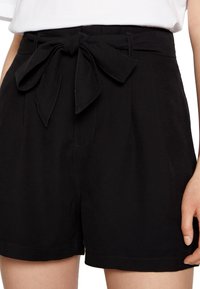 Schwarze Shorts mit einem Bindegürtel, Taschen und einem strukturierten Stoff. Der Bund ist verstärkt und hat gestickte Akzente entlang der Kanten.