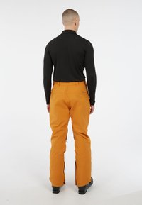 Oranje skibroek met een rechte snit, voorzien van ritsen bij de enkels en een hoge tailleband. Gemaakt van duurzaam, weerbestendig materiaal.