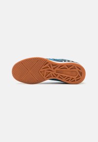 Zapatilla deportiva con una parte superior texturizada negra, acentos azules y una suela de goma con un patrón que presenta un diseño de cinta multi-direccional.