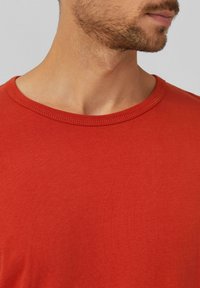 Rotes T-Shirt mit kurzen Ärmeln und rundem Halsausschnitt. Aus glattem Stoff gefertigt, mit einer schlichten Textur und sauberer Naht am Kragen.