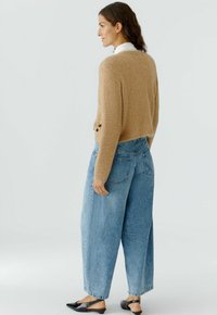 Beige, fuzzy trui met een ontspannen pasvorm, gecombineerd met hooggetailleerde, loszittende blauwe denim jeans. Zwarte platte schoenen maken de outfit af.