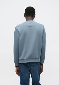Lys blå genser med rund hals og ribbestrikkede mansjetter, kombinert med blå denimjeans. Jevn stofftekstur med minimale detaljer.