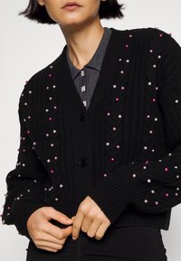Cardigan en tricot noir avec des embellissements en perles colorées, décolleté en V, poignets à côtes et fermeture par bouton.