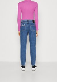 Smala blå jeans med en blekt textur, med två bakfickor och vita sömmar. Kombinerat med en figurnära, rosa långärmad tröja och svarta sneakers.