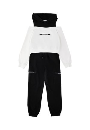 Felpa con cappuccio bianca e nera con la scritta "NEW ADVENTURE", abbinata a pantaloni cargo neri con la stessa scritta sulle tasche.